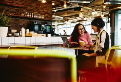 Two women chatting at a cafe with their laptop and coffee