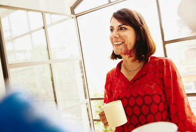 an image of a woman wearing a red blouse and holding a cup smiling while looking to the left