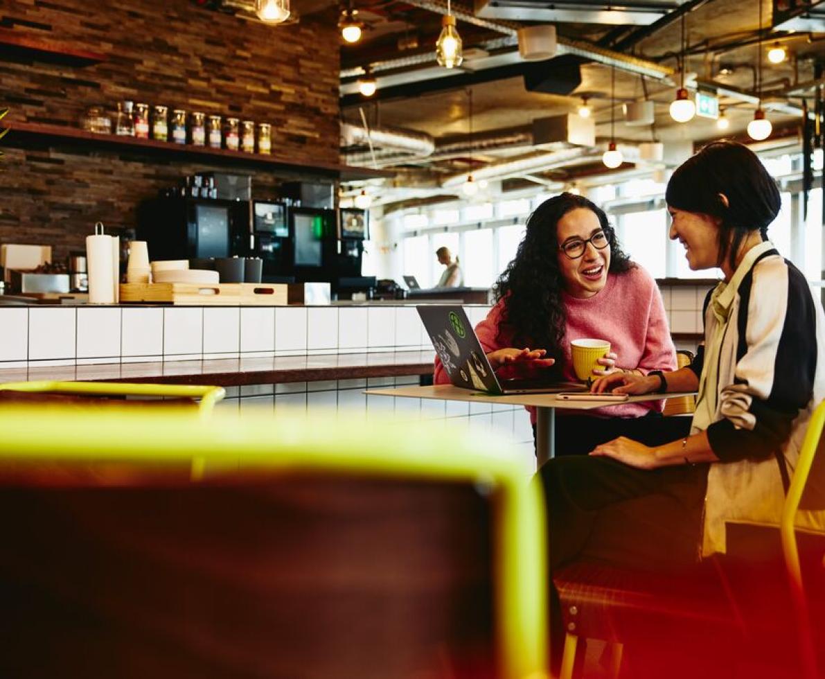 Two women chatting at a cafe with their laptop and coffee