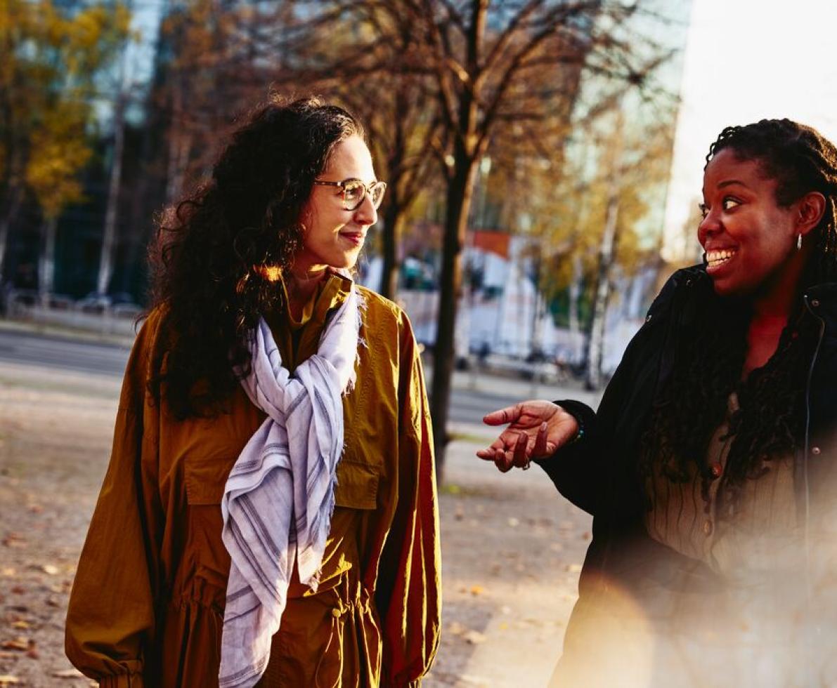 Two woman walking outside while having a conversation, smiling.