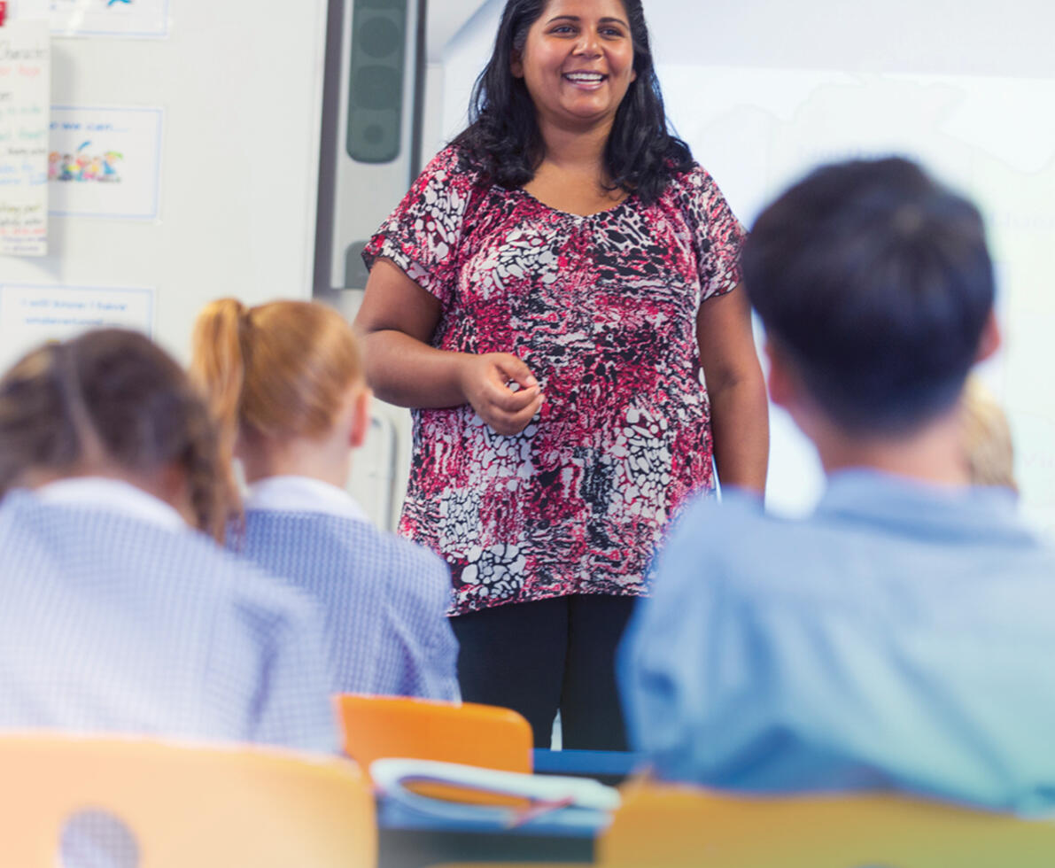 woman with dark hair smiling whilst she's teaching in a classroom with children