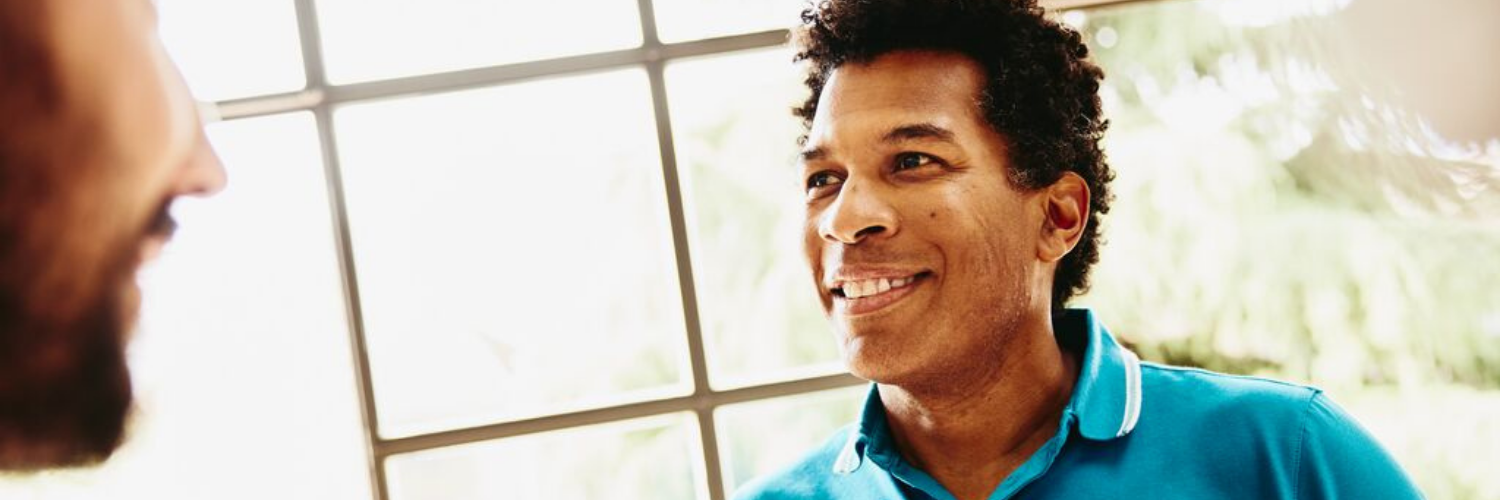 Smiling man holding a coffee cup having a chat with someone.