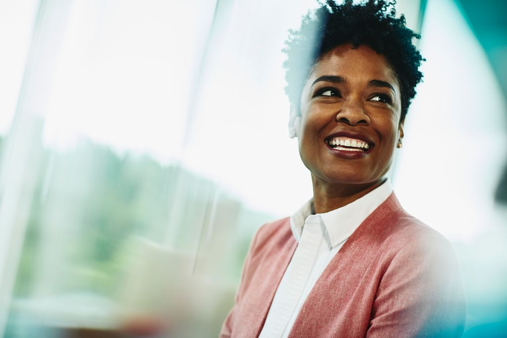 woman with black short hair in a pink blazer, white top, smiling with a faded green background