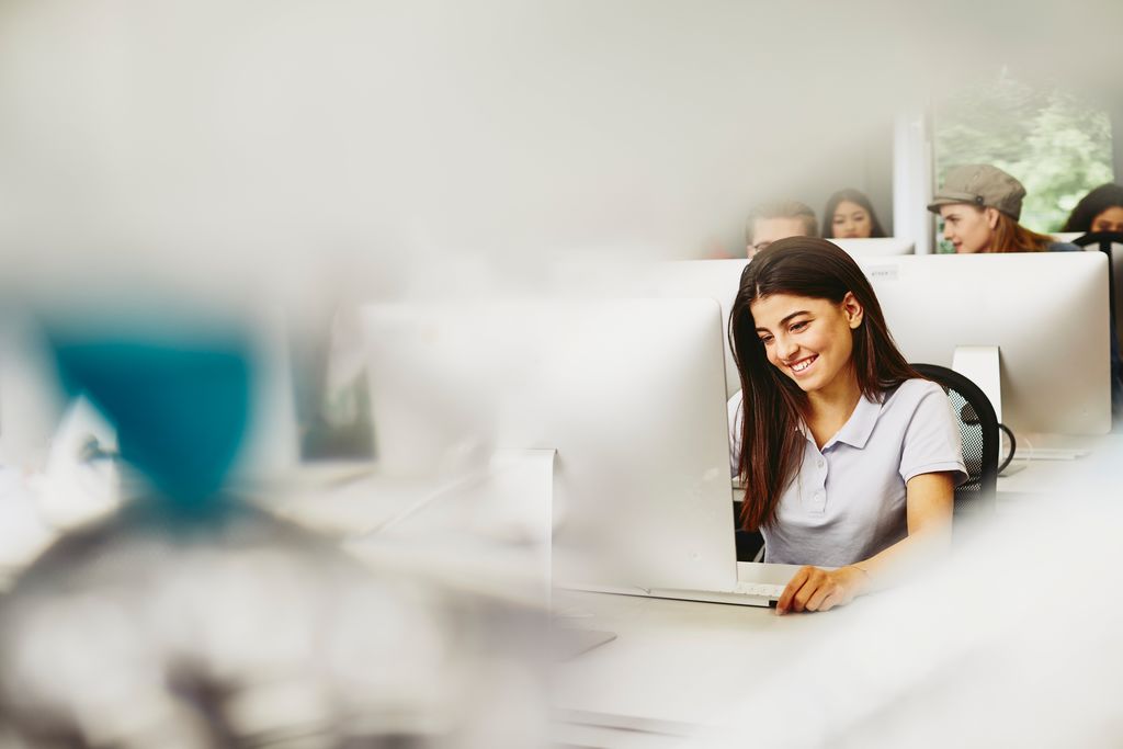 a woman wearing a white top sitting in front of a computer smiling 