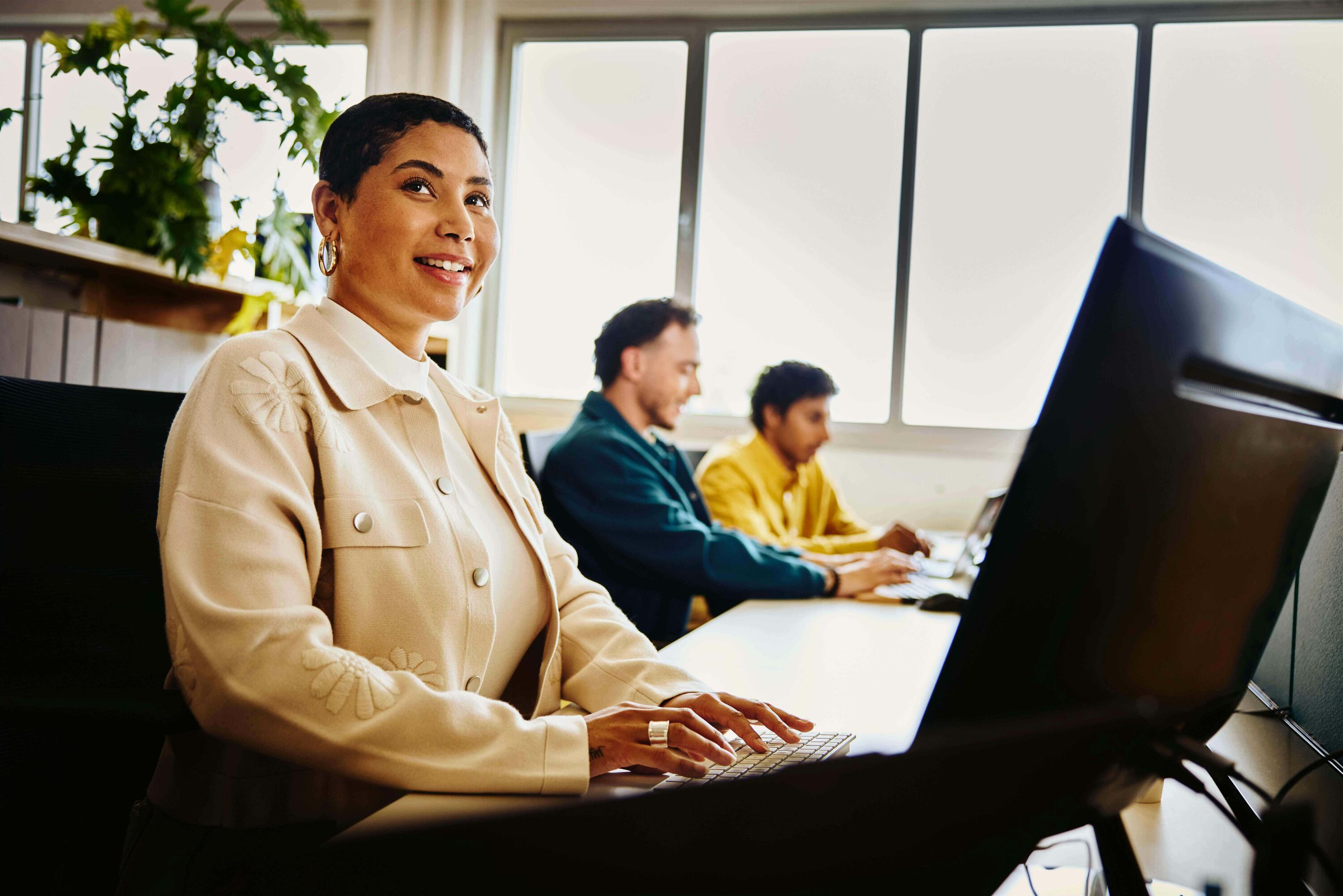 an image of a woman typing on her laptop while smiling brightly and looking at something to her far right 