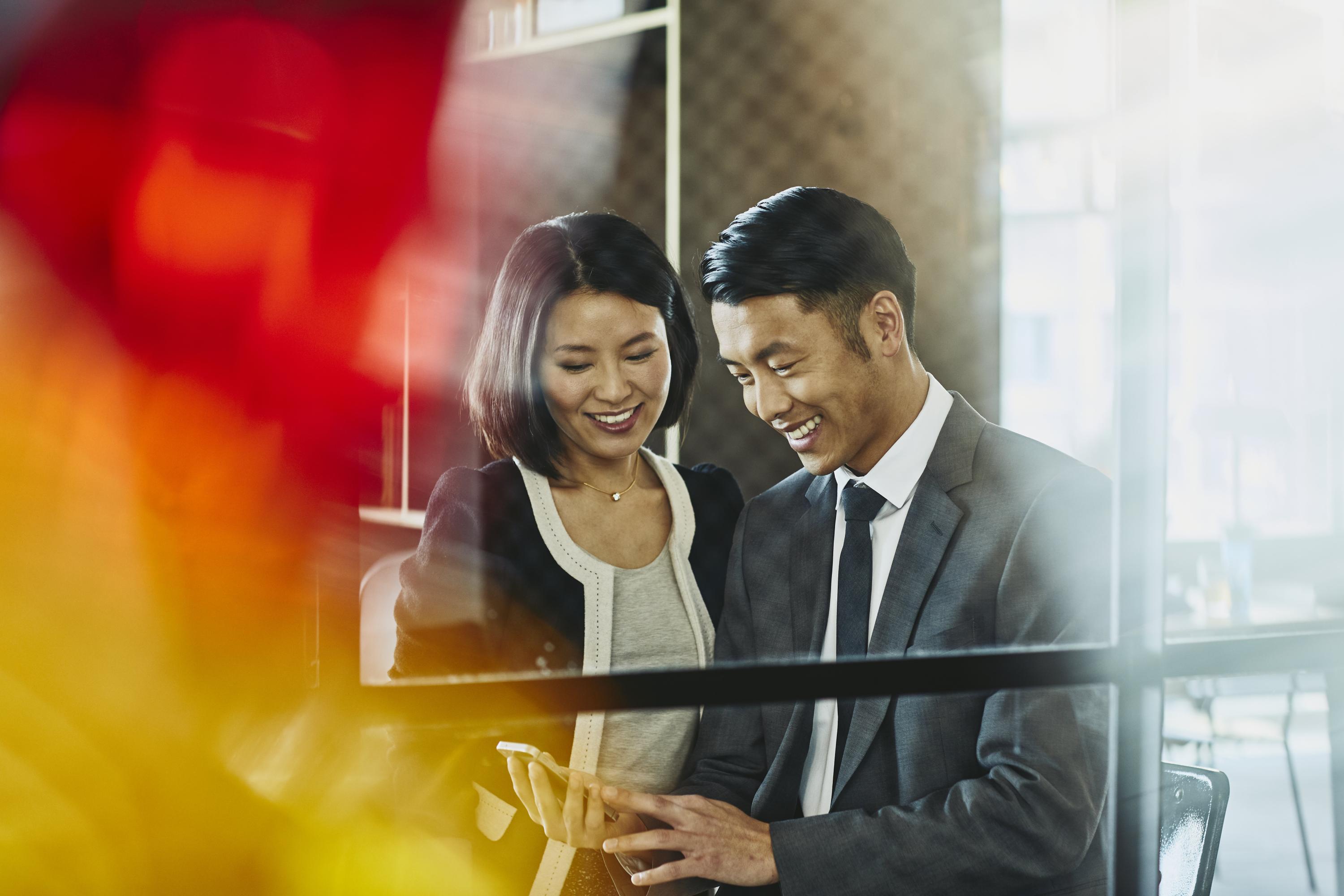 Man and woman looking at chell phone. China. Primary colors: red and yellow.