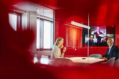 Man and woman in a meeting room with others on a video call