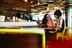 Two women chatting at a cafe with their laptop and coffee