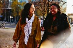 Two woman walking outside while having a conversation, smiling.