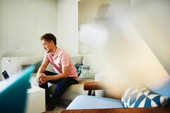 man in a pink shirt, sitting on his lounge, working from home. 