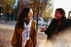 Two woman walking outside while having a conversation, smiling.