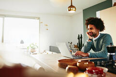  A man with a laptop resting his chin on his palm while smiling at something far away