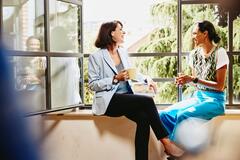 an image of two women chatting while sitting down on a window sill 