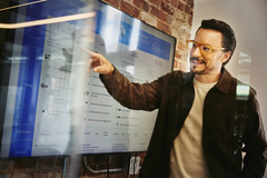 an image of a man with glasses pointing at a screen showing data while smiling
