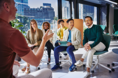 team of 5 people listening to a man presenting in an office with city views 