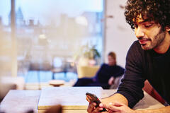 a man leaning on a kitchen bench looking at his mobile phone smiling
