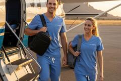 two travel nurses wearing scrubs exiting a small plane in a rural location