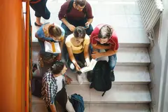 Closeup top view of group of college students waiting in a hallway for the class to begin class. They are sitting on the stairs and talking.
