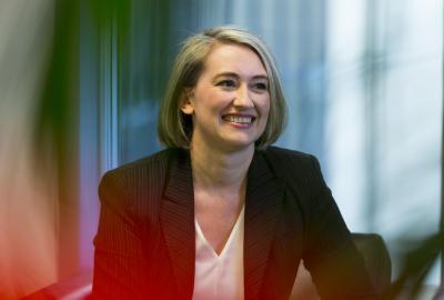 a blonde woman wearing a black coat smiling while looking to the right