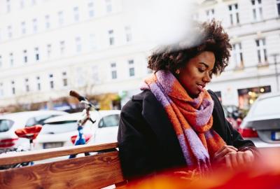 Woman looking at watch while sitting on a bench outside.