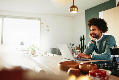  A man with a laptop resting his chin on his palm while smiling at something far away