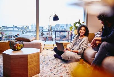 Woman with a laptop sitting on the floor and a man sitting on a couch