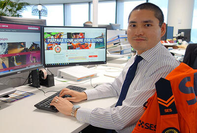 an image of a man sitting in his office desk, wearing a button up shirt and tie hands positioned in typing while looking at the camera