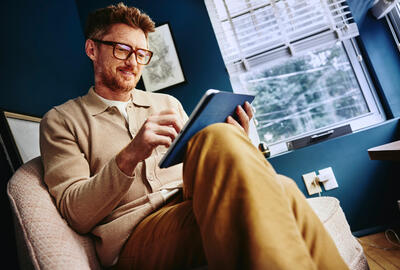 an image of a man wearing glasses and sitting on a chair while using his tablet 