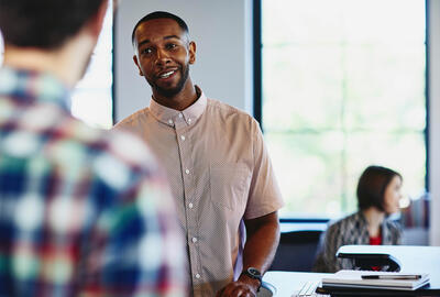 an image of a man talking to his coworker while smiling and a woman in the background working