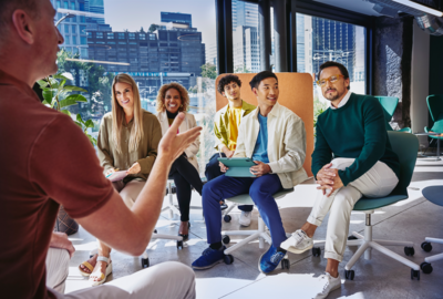 team of 5 people listening to a man presenting in an office with city views 