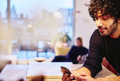 a man leaning on a kitchen bench looking at his mobile phone smiling
