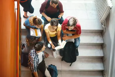Closeup top view of group of college students waiting in a hallway for the class to begin class. They are sitting on the stairs and talking.