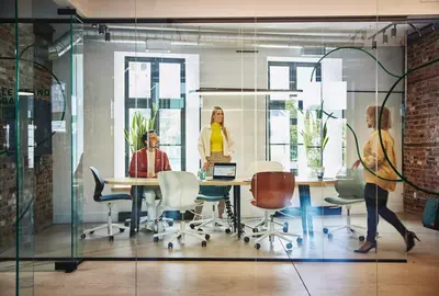 Female and male are sitting and female is standing at a table in a office meeting room