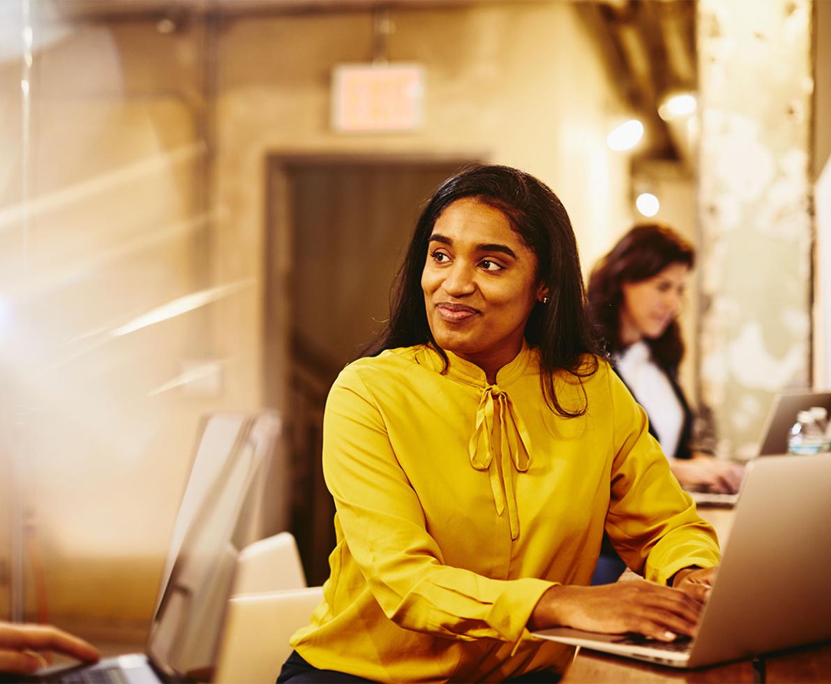 Woman in yellow typing on her laptop