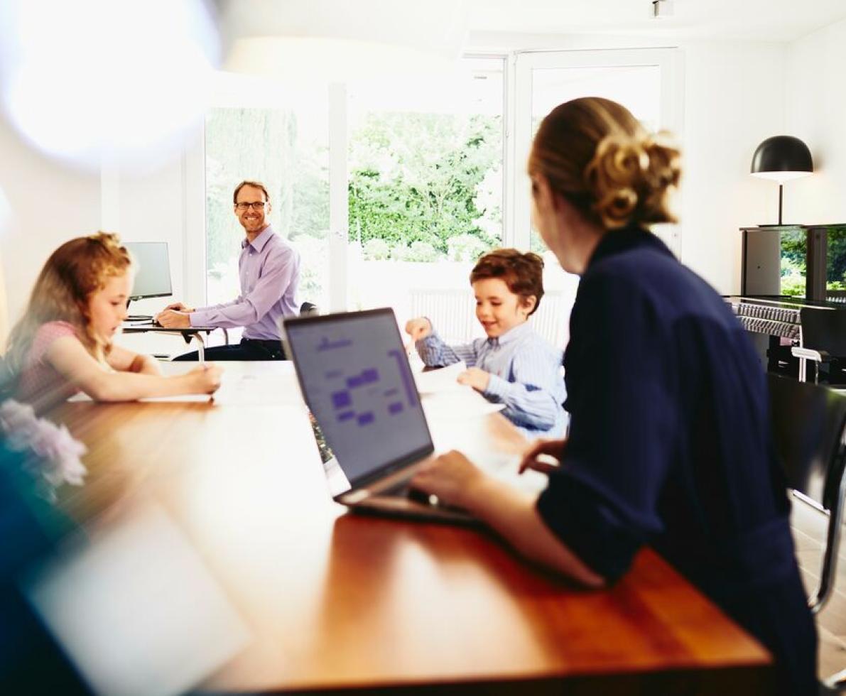 Woman working from home with her family in the background Woman working from home with her family in the background