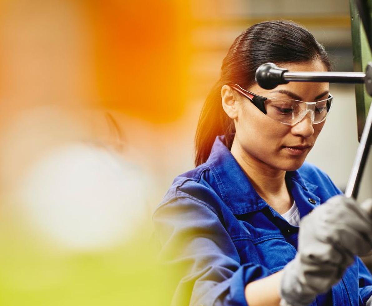 Female factory worker operating a column drill. Asian woman wearing safety goggles and protection gloves. Hair in a ponytail.
