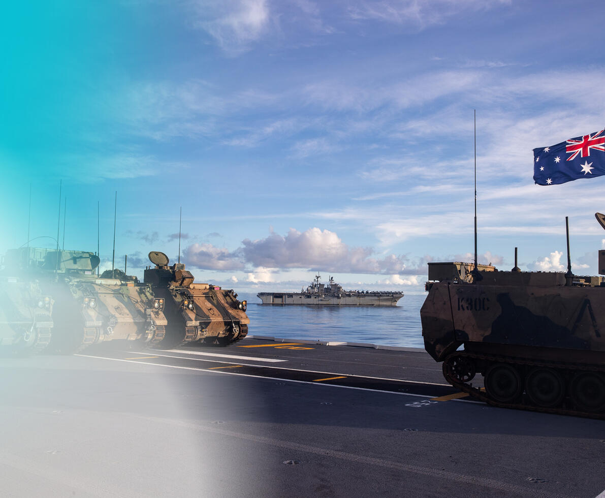 A photo of army tanks at a port with a naval ship from afar A photo of army tanks at a port with a naval ship from afar