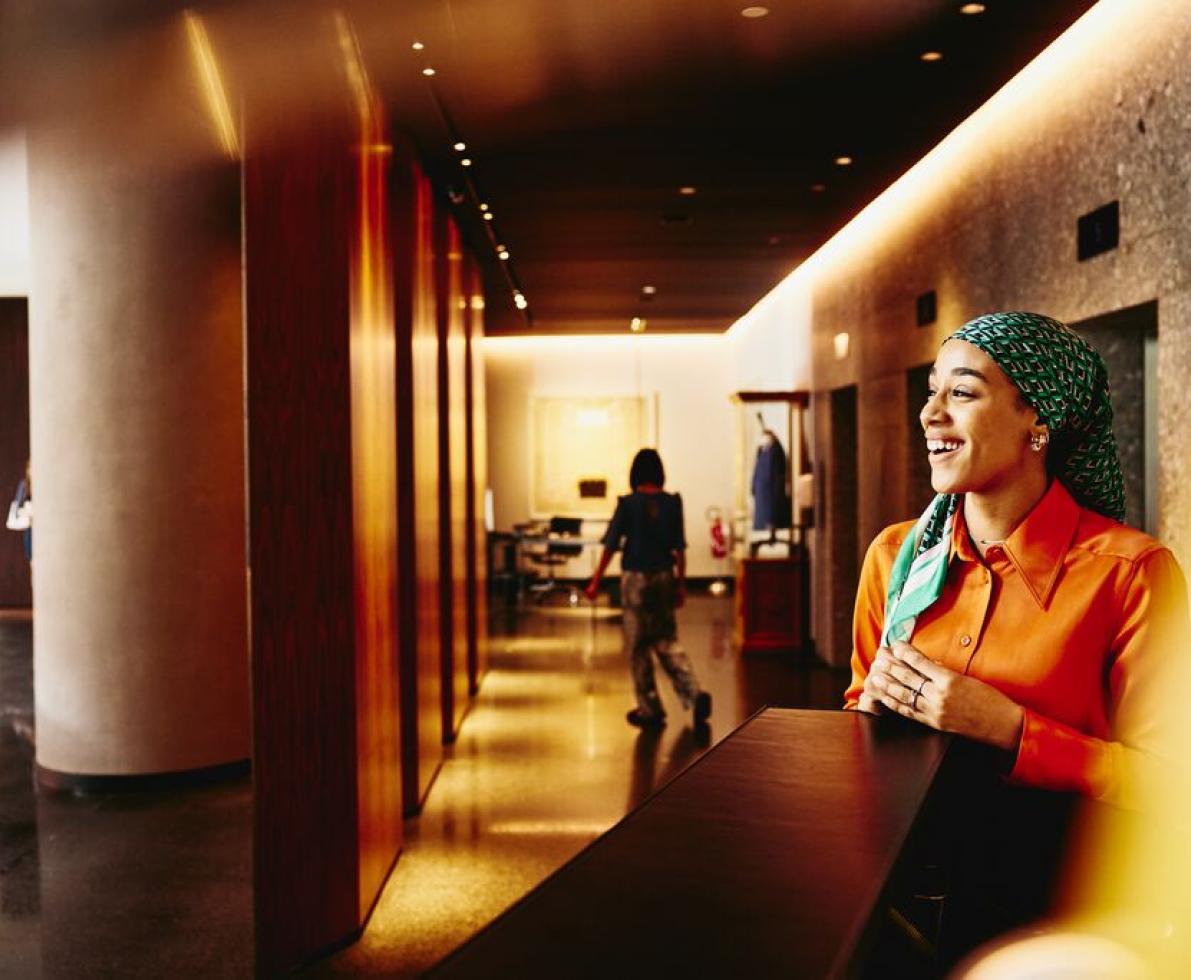 Smiling woman receptionist standing next to hotel reception desk.