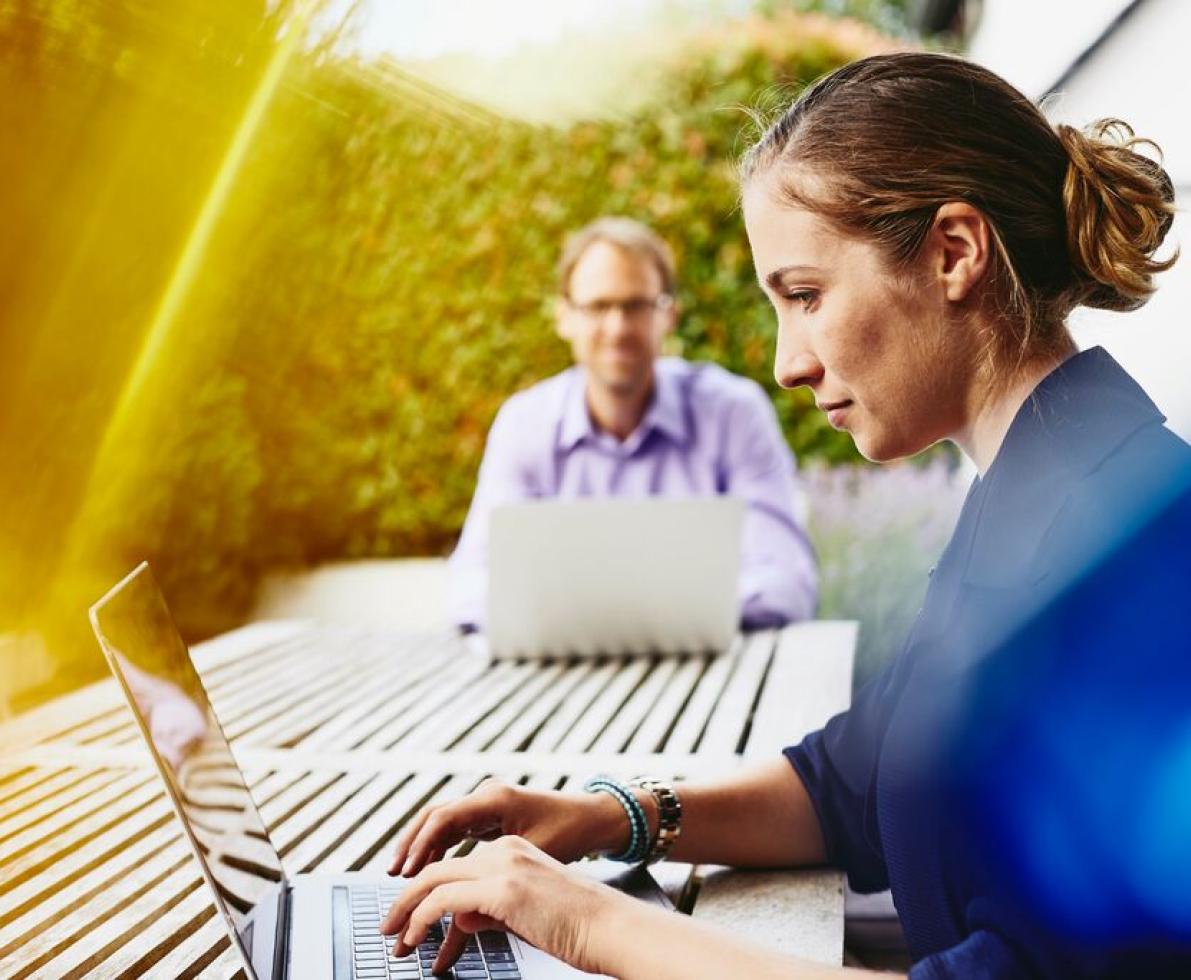 Focused man and woman working on their laptop and sitting at a table in a garden.