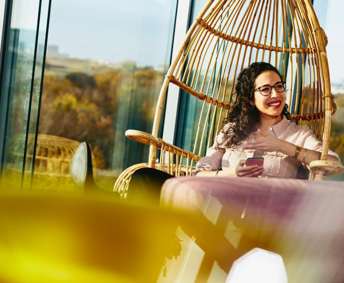 Woman smiling looking away while sitting down and holding her phone.