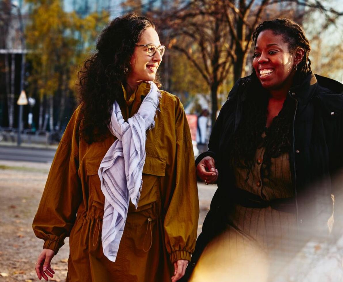 Two woman walking outside while having a conversation, smiling.