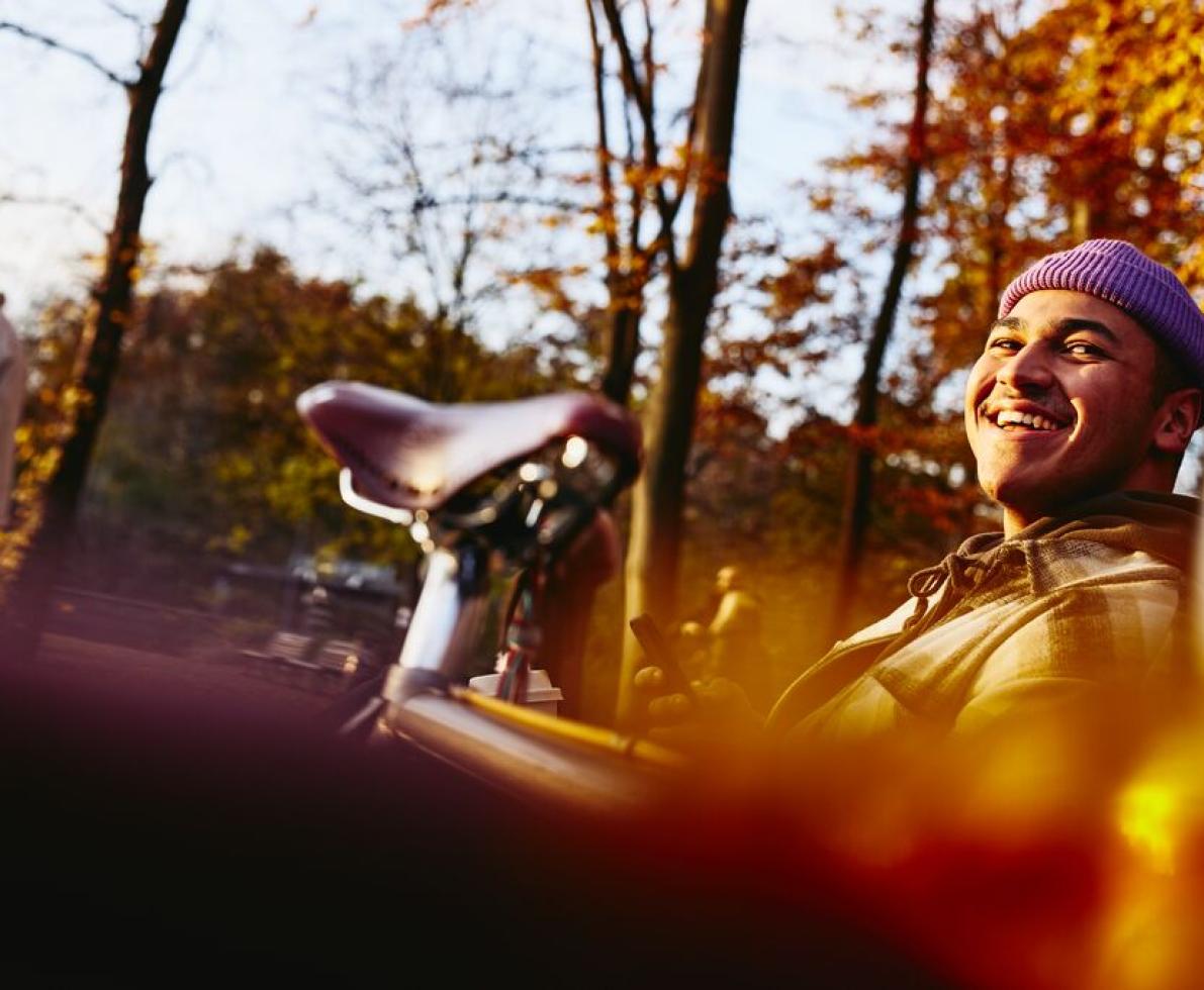 Smiling man sitting on a bench with his bike next to him, looking up while holding his phone.