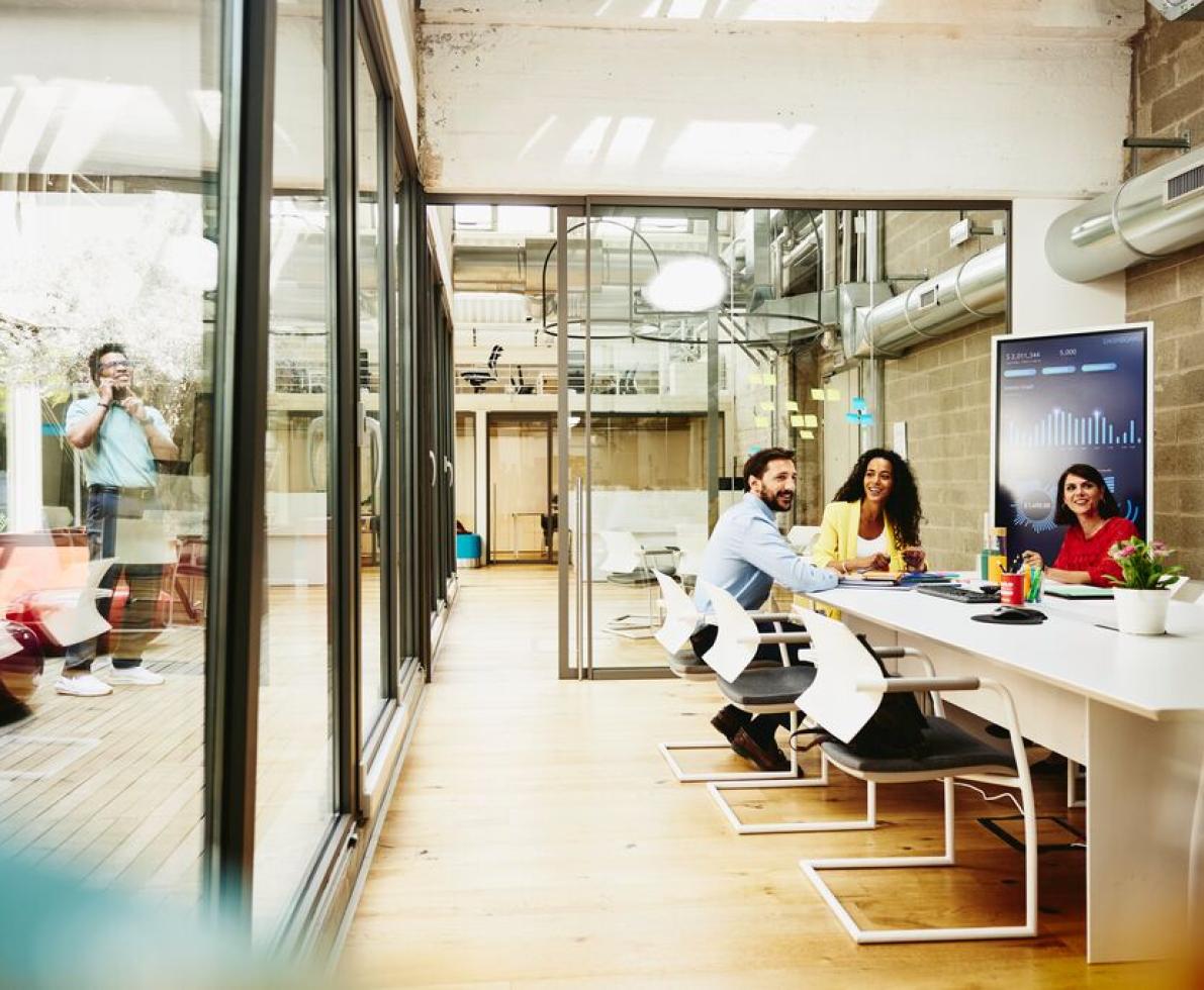 Group of office workers in a conference room while a man is on the phone outside 