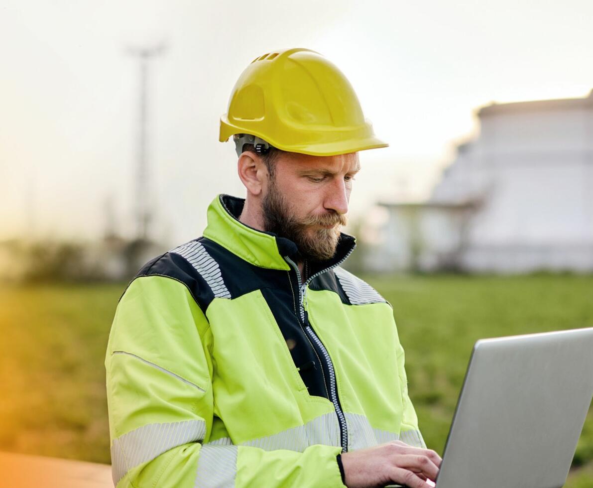 a man wearing a yellow hardhat and construction uniform looking at his laptop