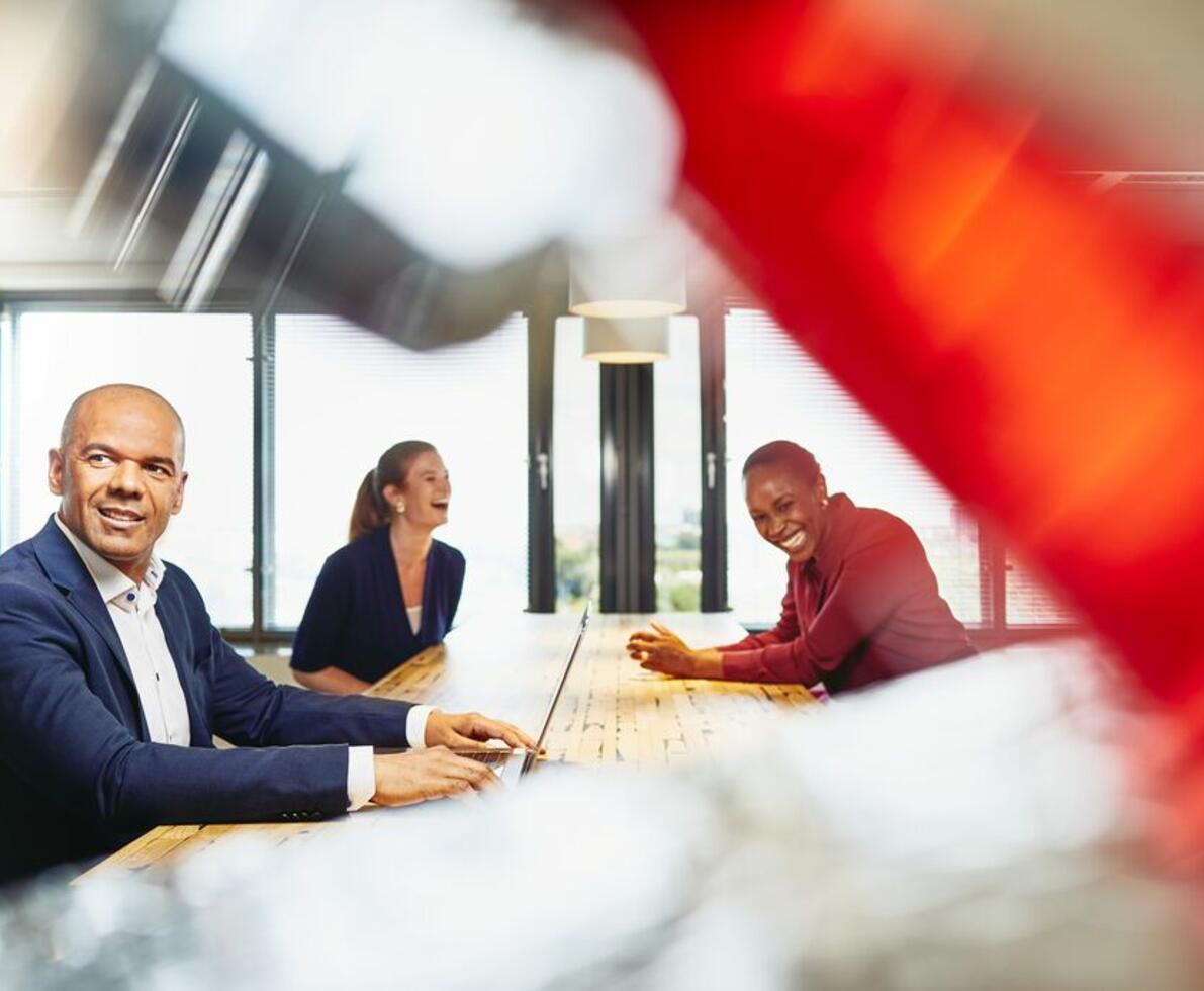 Man working on his laptop, in the background two women having fun and laughing
