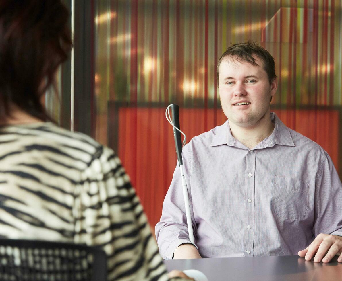 man with guide cane at an interview with a woman at desk 
