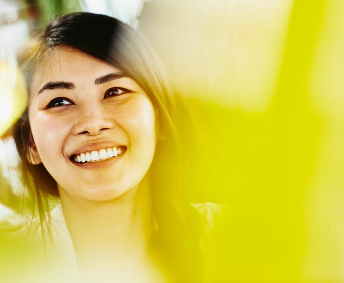 woman with dark coloured haired looking up smiling with a yellow filter