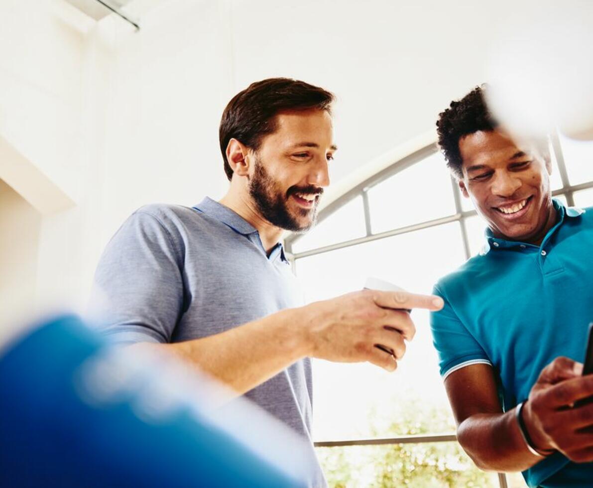 two men talking together while smiling and looking at a mobile device held by one of them. 