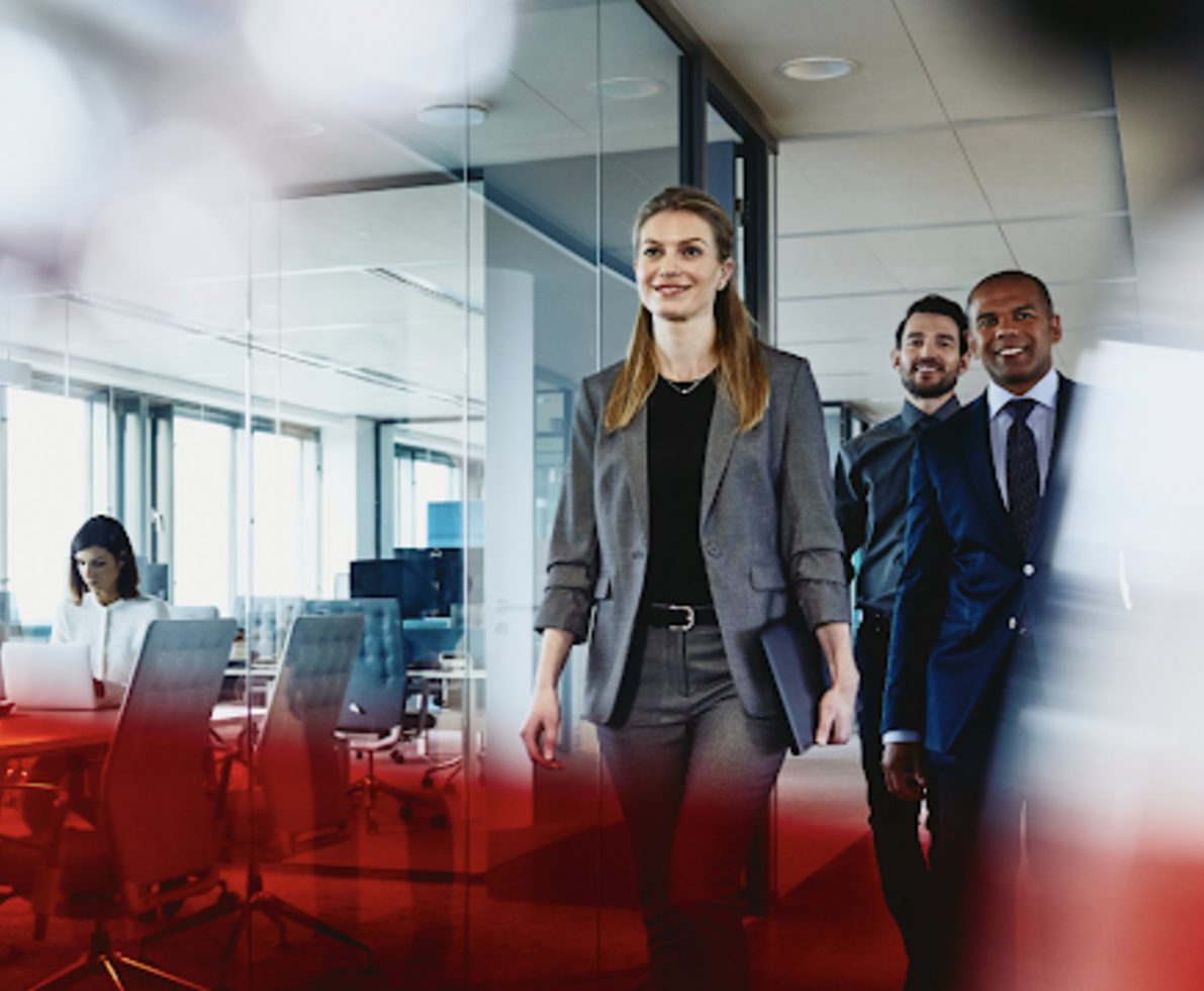 a lady and two men all in suits, walking in a corporate office smiling 