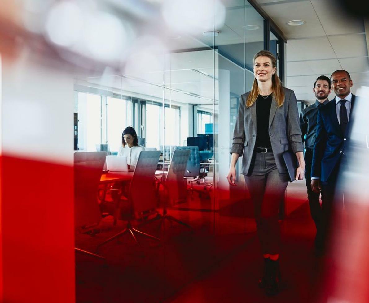 Woman in a business suit walking in the office with her coworkers behind her